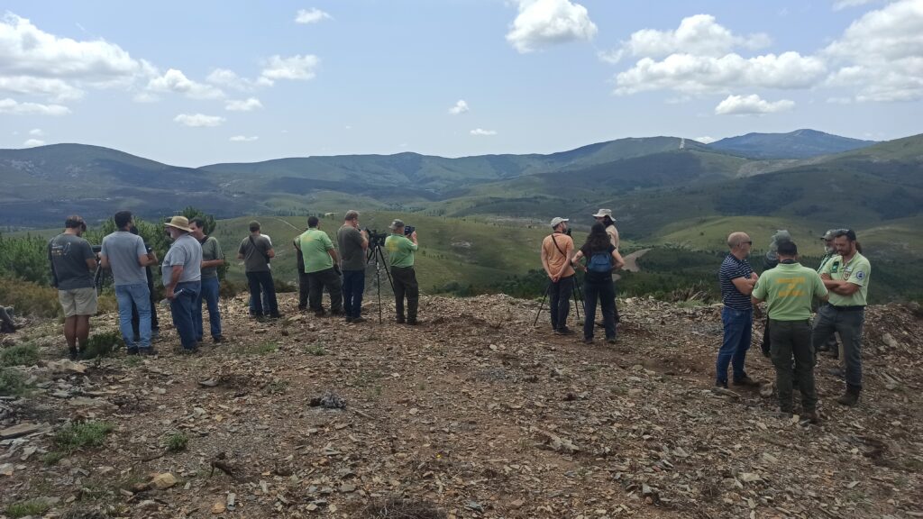 a group of people scattered around binoculars and other monitoring tools, on top on a hill and facing portuguese landscape