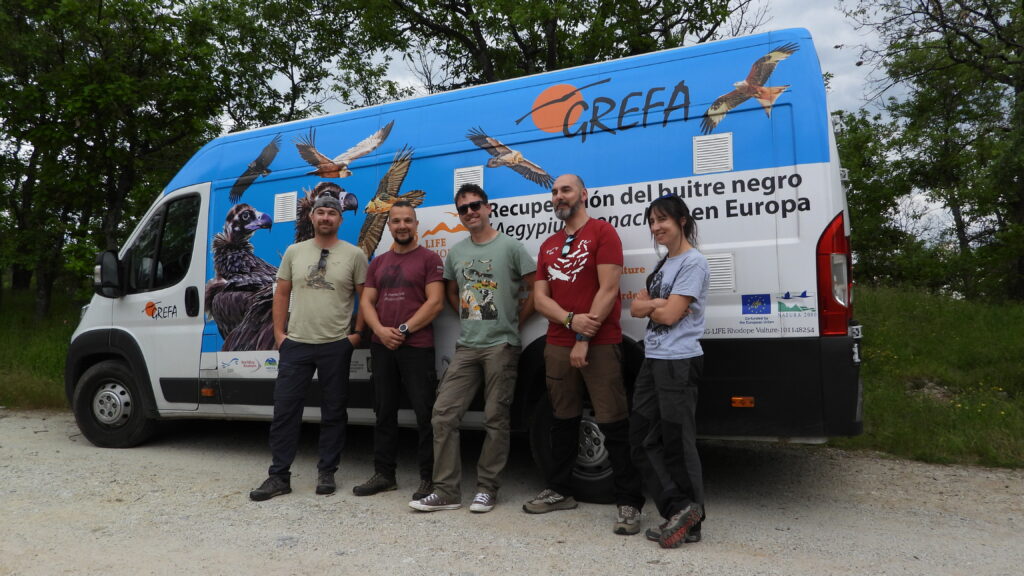 Four men and an woman standing in front of a van smiling.